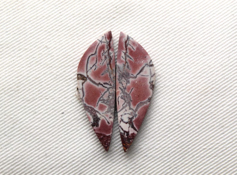 May include: Two matching teardrop-shaped cabochons featuring a polished surface with a deep reddish-brown base color and intricate, dark grey to black veining patterns that create a web-like appearance across the stone faces.