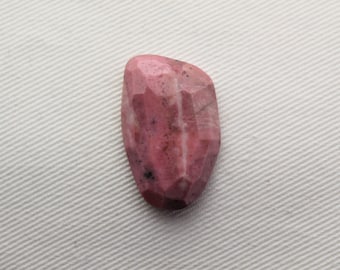 May include: A faceted, polished gemstone in shades of pink and rose. The stone has a unique shape with a flat back and a rounded, textured front. The gemstone is likely a cabochon, suitable for jewelry making.