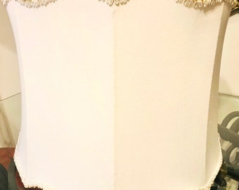 May include: A white lampshade with a scalloped edge and a gold trim. The lampshade is made of a soft, fabric material.