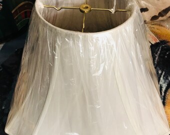 May include: A white lampshade with a square shape and a pleated design. The lampshade is made of fabric and has a metal frame.