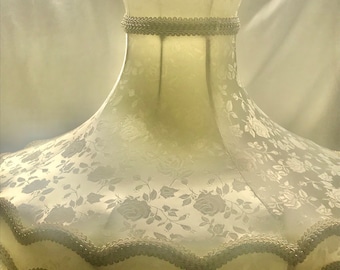 May include: A white lampshade with a floral pattern and a scalloped edge. The lampshade has a cream-colored fringe around the bottom.