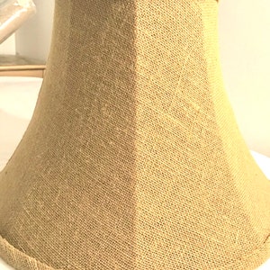 May include: A beige lampshade made of burlap fabric with a slightly textured surface.