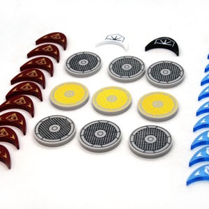 Op de afbeelding: Een set spelstukken, waaronder 10 rode, 10 blauwe en 10 grijze plastic tokens. Er zijn ook drie gele, twee zwarte en twee witte tokens. De tokens zijn allemaal in verschillende vormen en maten.