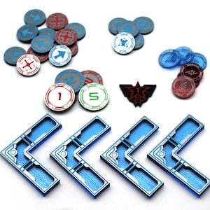 May include: A collection of game components including four blue L-shaped plastic frames with textured surfaces, various circular tokens in red, blue, and white featuring arrows, numbers, and symbols, and one black triangular emblem with a red number one.
