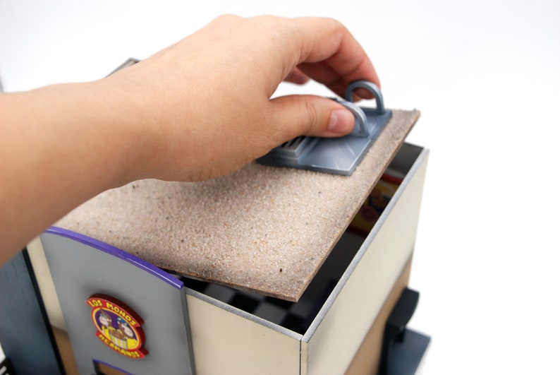 K&ouml;nnte beinhalten: Ein Miniatur-Geb&auml;udemodell mit abnehmbarem Dach. Das Geb&auml;ude hat eine violette und graue Au&szlig;enfassade mit einem Schild, auf dem "Lollipop Ice Cream Parlor" steht. Das Dach besteht aus einem braunen Material mit einer strukturierten Oberfl&auml;che.