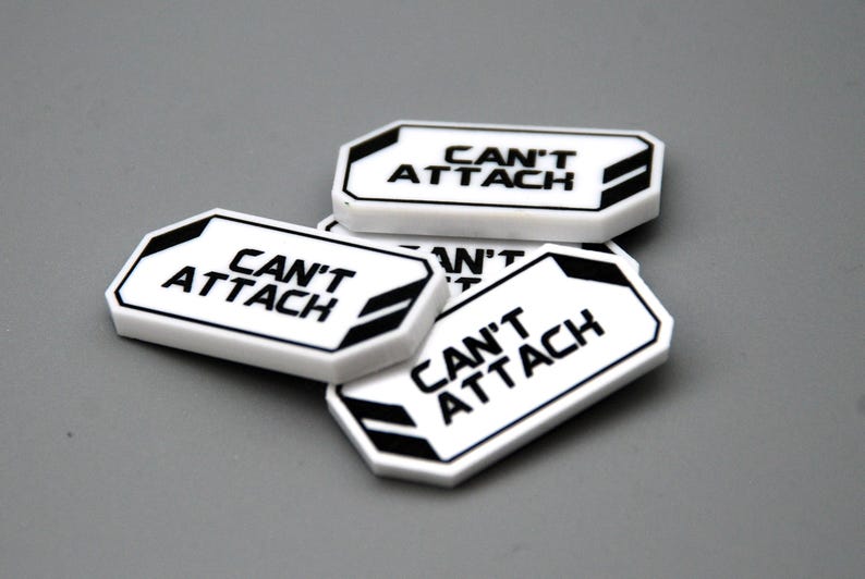 May include: A collection of white rectangular plastic tags with beveled corners, each featuring the black text CAN'T ATTACH printed in the center. The tags have a black border and black geometric accents on the left and right sides.