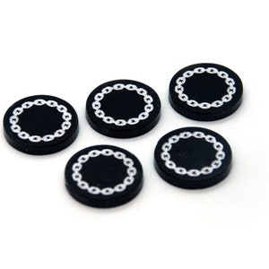 May include: Five black poker chips with a silver chain design around the edge.