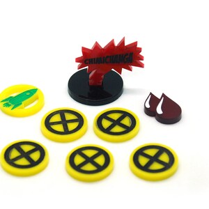 Puede incluir: Un conjunto de piezas de juego, que incluyen fichas amarillas con miras negras, una explosión roja con el texto "CHIMICHANGA", un cohete verde y formas de gotas de sangre granate. Las piezas están sobre un fondo blanco.