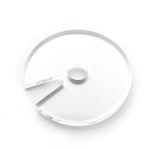 Puede incluir: Un disco de plástico transparente con un agujero en el centro y una sección recortada. El disco tiene un diámetro de aproximadamente 7,5 cm.