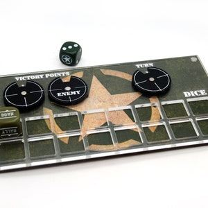 Puede incluir: Un tablero de juego de acrílico transparente con un patrón de camuflaje verde y marrón. El tablero tiene una estrella en el centro y espacios para dados, puntos de victoria y fichas enemigas. El tablero también tiene las palabras "Victory Points", "Enemy", "Turn", "Dice" y "Down" impresas en él.