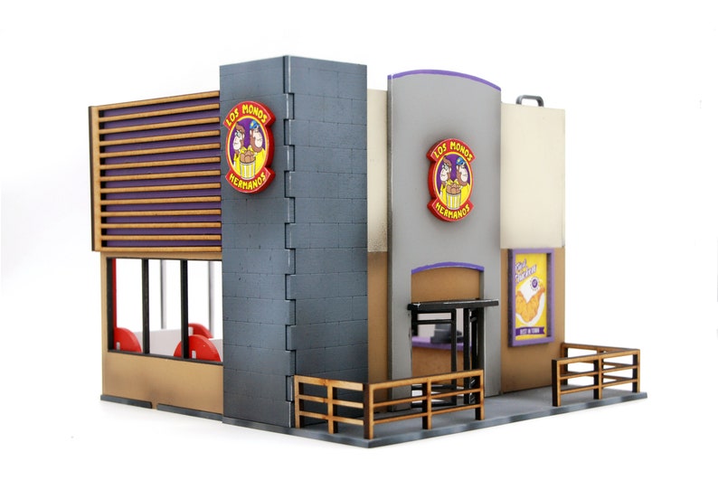 K&ouml;nnte beinhalten: Ein Miniaturmodell eines Restaurants namens "Los Monos Hermanos" mit einer lila-wei&szlig;en gestreiften Markise, einem gro&szlig;en Fenster und einem Schild mit dem Namen und dem Logo des Restaurants. Das Modell ist aus Holz gefertigt und hat ein detailliertes &Auml;u&szlig;eres.