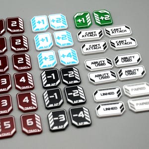 May include: A collection of game tokens featuring various colors and text. The set includes maroon DMG tokens, light blue AP tokens, green HP tokens, and white tokens labeled CAN'T ATTACH, ABILITY USED, LINKED, and PAIRED with black and white accents.