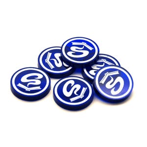 Peut inclure: Un ensemble de six jetons circulaires bleus avec une bordure blanche et un motif graphique central blanc représentant une lettre S stylisée combinée à une icône de livre ouvert. Les jetons sont empilés en un petit tas sur un fond blanc.