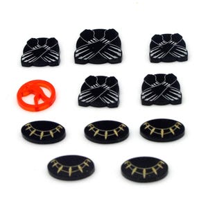 Könnte beinhalten: Ein Satz schwarzer und goldener Spielsteine mit einem Friedenszeichen in der Mitte. Die Steine zeigen ein schwarzes Panther-Design und ein goldenes Halsband-Design.