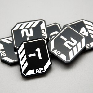 May include: A collection of black, octagonal game tokens featuring white printed graphics. Each token displays a numerical value, such as -1, -2, or 4, alongside the text AP and white diagonal striped accents on the corners of the game pieces.