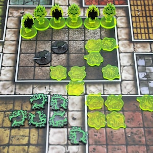 Può includere: Un tabellone di gioco con vari pezzi. I pezzi includono figure traslucide verdi, gettoni circolari neri e forme di vite verdi. Il tabellone ha un motivo a griglia con quadrati marroni e grigi.