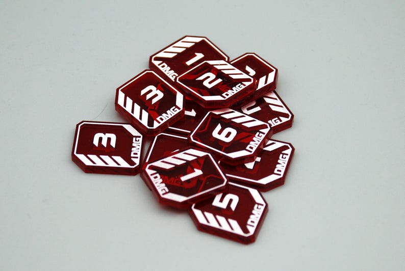 May include: A collection of translucent red acrylic tokens, each octagonal in shape with white printed numbers and the text DMG. The tokens feature white diagonal stripes in the corners and display various numerical values including 1, 2, 3, 5, and 6.
