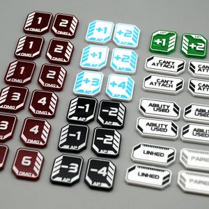 May include: A collection of game tokens featuring various designs. Dark red tokens are marked with numbers 1 through 6 and DMG. Light blue tokens show +1, +2, +3, +4 and AP. Black tokens show -1, -2, -3, -4 and AP. White tokens display CAN'T ATTACH, ABILITY USED, LINKED, or PAIRED.