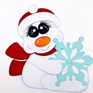 May include: A whimsical snowman cutout, approximately 4 inches tall and 4.5 inches wide, wearing a red hat and scarf, holding a light blue snowflake. The snowman has large black eyes, an orange carrot nose, and rosy cheeks. The text "Scrappin' Heaven" is at the bottom.