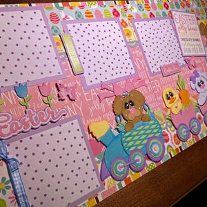 May include: A scrapbook page with an Easter theme. It features photo frames with purple polka dots, decorative cutouts of flowers, butterflies, and a train carrying Easter characters. The word "Easter" is prominently displayed.