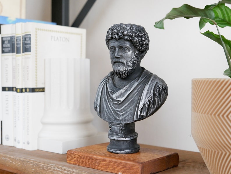 Puede incluir: Un busto de plata de un hombre con barba y pelo rizado sobre una base de madera. El busto est&aacute; en un estante con libros y una planta en una maceta.
