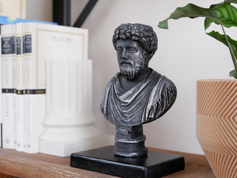 Puede incluir: Un busto de plata de un hombre con barba y pelo rizado. El busto est&aacute; sobre una base negra y se encuentra en un estante de madera con libros y una planta.