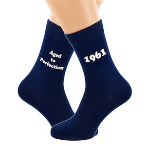 Pode incluir: Um par de meias azul marinho com texto branco. Uma meia diz "Aged to Perfection" e a outra diz "1961".