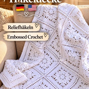 Puede incluir: Una manta de ganchillo blanca con motivos cuadrados que presentan intrincados patrones florales y texturas en relieve. El texto en la imagen dice: Anleitung Häkeldecke, Reliefhäkeln y Embossed Crochet, junto a iconos de banderas alemana y estadounidense.