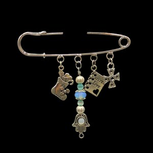 May include: Silver safety pin with charms including a stocking, a hamsa hand, a cross, and a tag that says "Secret Love".
