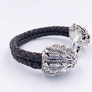 K&ouml;nnte beinhalten: Ein schwarzes geflochtenes Lederarmband mit silbernen Adlerkopf-Verschl&uuml;ssen.