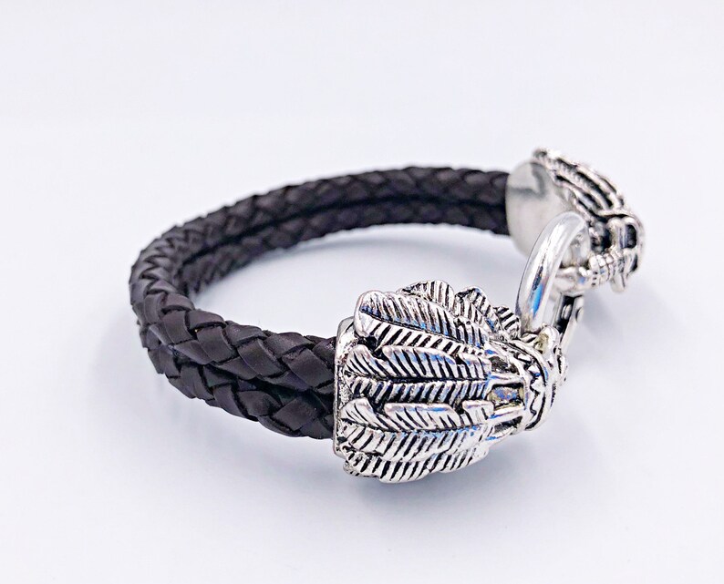 K&ouml;nnte beinhalten: Ein schwarzes geflochtenes Lederarmband mit silbernen Adlerkopf-Verschl&uuml;ssen.