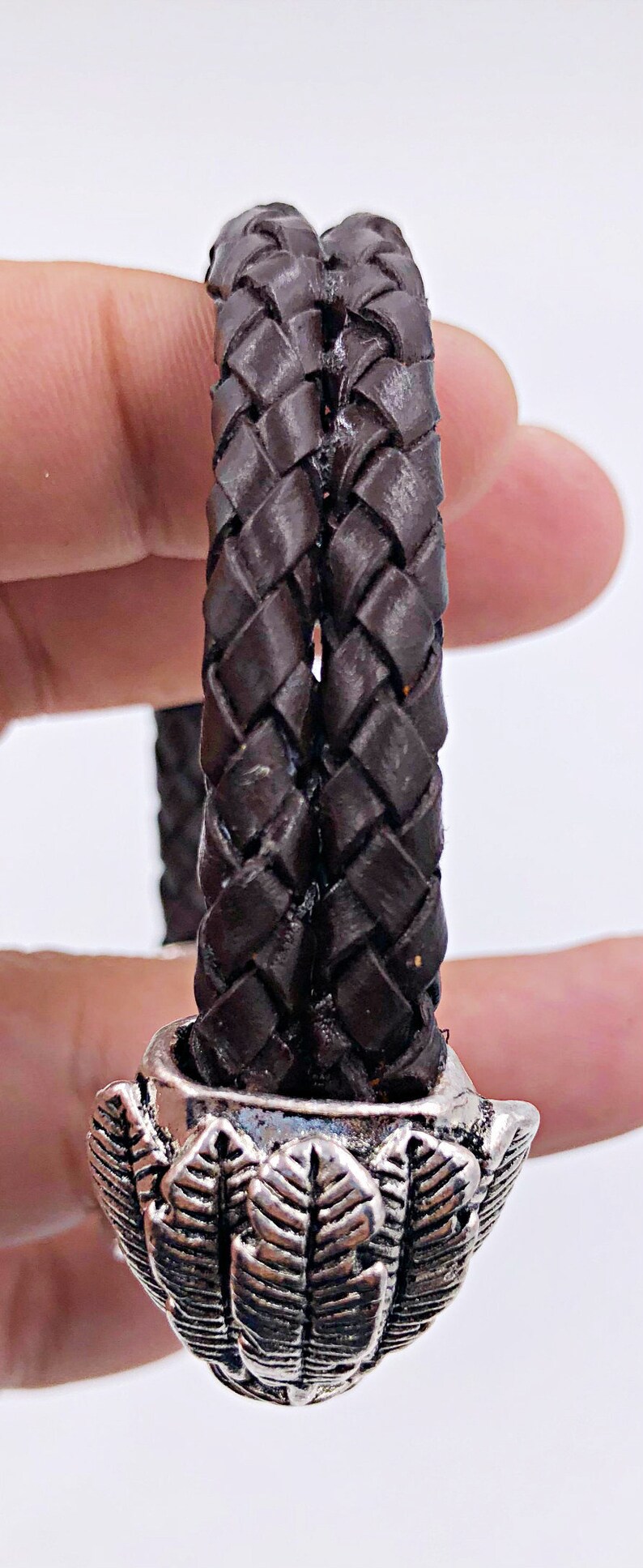 K&ouml;nnte beinhalten: Ein braunes Lederarmband mit einem silbernen, blattartigen Verschluss.