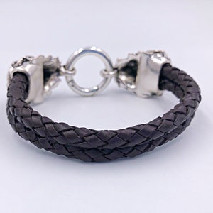 K&ouml;nnte beinhalten: Ein braunes Lederarmband mit silbernen Totenkopf-Akzenten und einem runden Verschluss.