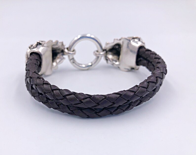 K&ouml;nnte beinhalten: Ein braunes Lederarmband mit silbernen Totenkopf-Akzenten und einem runden Verschluss.