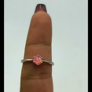 May include: A silver ring with a pink opal gemstone. The ring is on a finger.