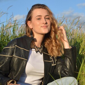 Puede incluir: Chaqueta de cuero negro con rayas color crema y un parche con el n&uacute;mero 1. La chaqueta se lleva sobre una camiseta blanca y combinada con vaqueros azules. La modelo lleva un collar y pendientes de cuentas negras.