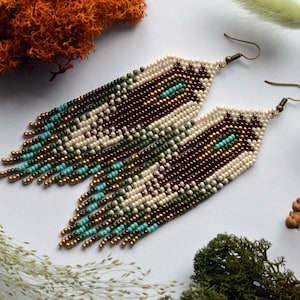 May include: A pair of long, beaded earrings with a geometric pattern in shades of brown, green, and turquoise. The earrings are made with small, seed beads and have a fringe-like design.