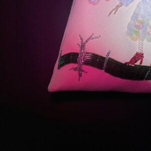 Puede incluir: Primer plano de una almohada bordada en rosa y blanco con un dise&ntilde;o de cuentas de un &aacute;rbol y una figura con zapatos rojos.