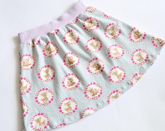 May include: A light blue skirt with a white background and a pink and brown deer print. The skirt has a lavender elastic waistband.
