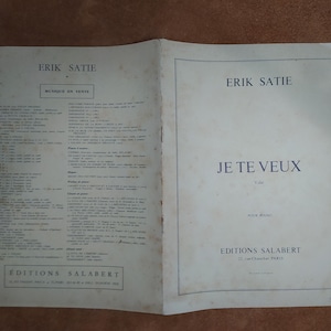 May include: A vintage sheet music booklet for Erik Satie's Je Te Veux, featuring a cream-colored cover with dark blue text. The front displays the title, composer, and Editions Salabert publisher details, while the back lists musical works.
