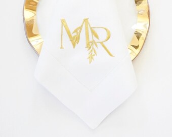 May include: White linen napkin with gold embroidered initials "MR" and a leafy design.