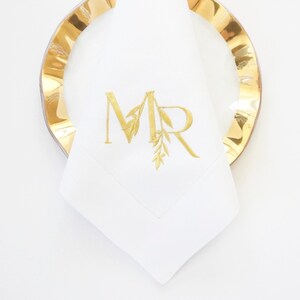 May include: White linen napkin with gold embroidered initials "MR" and a leafy design.