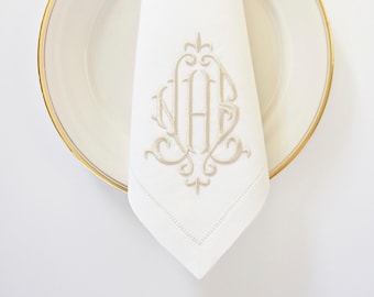 May include: A white linen napkin with a gold embroidered monogram "HAS" on a white plate with a gold rim.