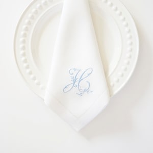 May include: White linen napkin with a blue embroidered initial "H" with a floral design.