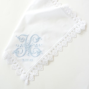 Peut inclure: Mouchoir en coton blanc avec une initiale brodée en bleu "K" et la date "9.27.25" entourée de motifs floraux délicats. Le mouchoir a une bordure en dentelle blanche.