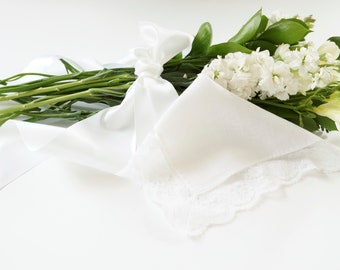 May include: A bouquet of white flowers wrapped in a white fabric with a lace trim and tied with a white satin ribbon.