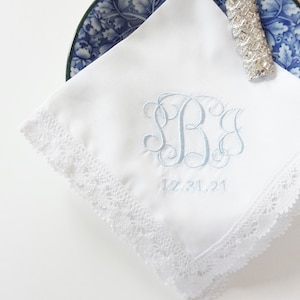 May include: White handkerchief with a blue embroidered monogram and the date 12.31.21. The handkerchief has a white lace trim.
