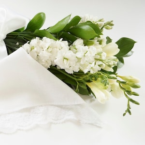 May include: A white lace handkerchief tied with a white satin ribbon and a bouquet of white and cream flowers.