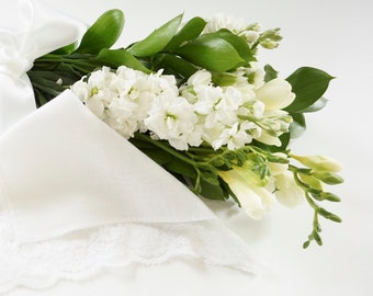 May include: A white lace handkerchief tied with a white satin ribbon and a bouquet of white and cream flowers.