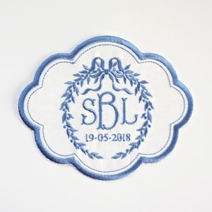 May include: A white embroidered patch with a blue floral wreath, the initials "SBL" and the date "19-05-2018".